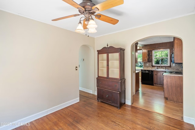 spare room with arched walkways, a ceiling fan, light wood finished floors, a sink, and baseboards