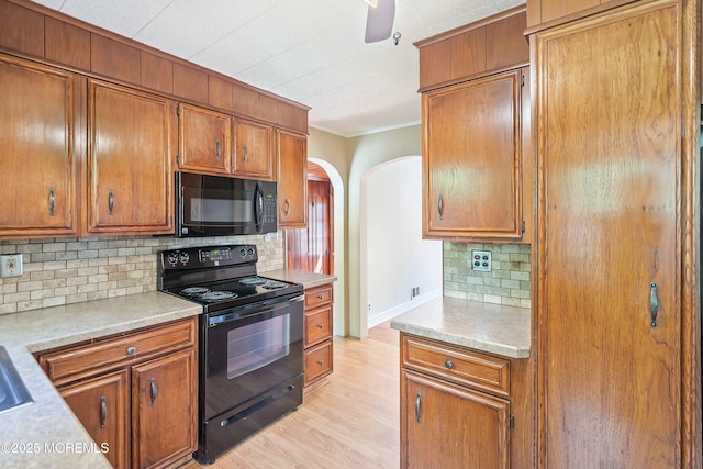 kitchen featuring black appliances, arched walkways, crown molding, tasteful backsplash, and light countertops