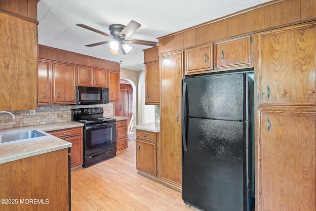 kitchen featuring black appliances, a sink, tasteful backsplash, brown cabinetry, and light countertops
