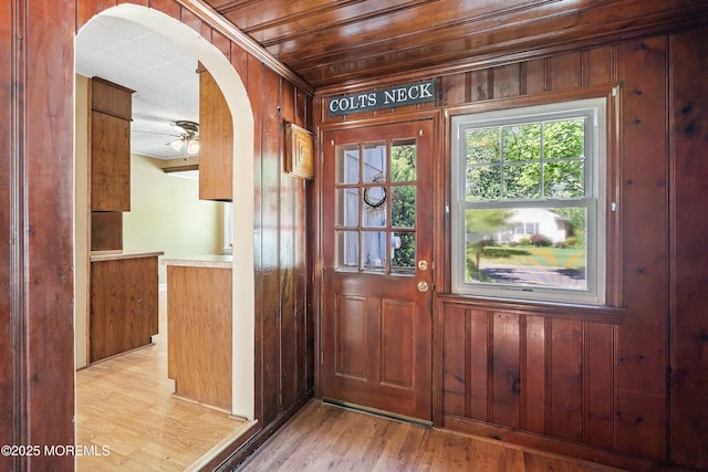entryway featuring wood walls, arched walkways, light wood-type flooring, ornamental molding, and ceiling fan