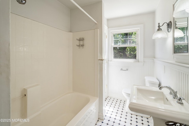 bathroom with toilet, a wainscoted wall, tile patterned flooring, shower / bathtub combination, and a sink