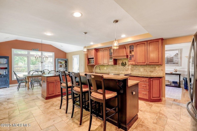 kitchen featuring glass insert cabinets, brown cabinets, a kitchen breakfast bar, a kitchen island with sink, and premium range hood