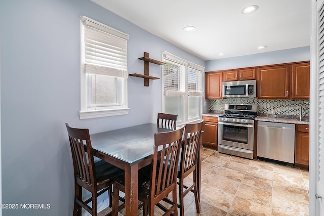 kitchen featuring stainless steel appliances, tasteful backsplash, brown cabinets, light stone finish flooring, and recessed lighting