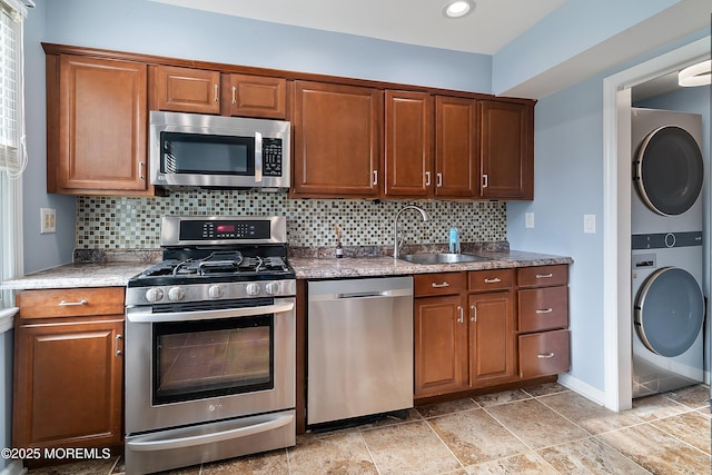 kitchen with appliances with stainless steel finishes, a sink, stacked washer / drying machine, tasteful backsplash, and brown cabinetry