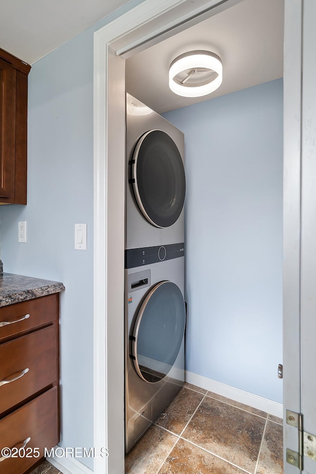 washroom with stacked washer and clothes dryer, baseboards, and stone tile flooring