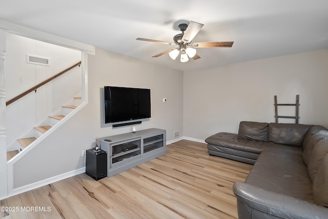 living room with wood finished floors, ceiling fan, baseboards, and stairs