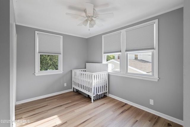 bedroom featuring crown molding, wood finished floors, baseboards, ceiling fan, and a nursery area