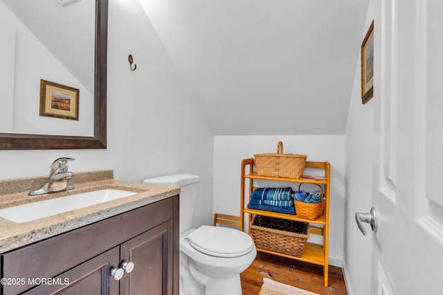 half bathroom featuring vanity, vaulted ceiling, toilet, and wood finished floors