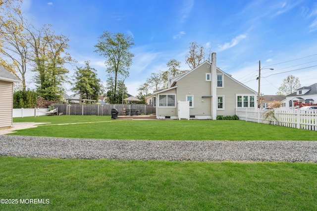 rear view of house featuring a fenced backyard, a chimney, and a yard