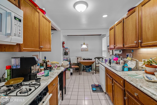 kitchen with light tile patterned floors, a sink, brown cabinetry, white appliances, and decorative backsplash