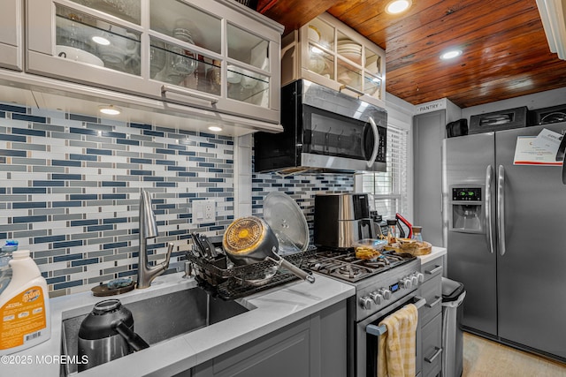 kitchen with glass insert cabinets, wooden ceiling, decorative backsplash, stainless steel appliances, and gray cabinets
