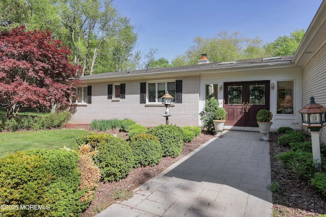 view of front of home with brick siding, french doors, and a chimney