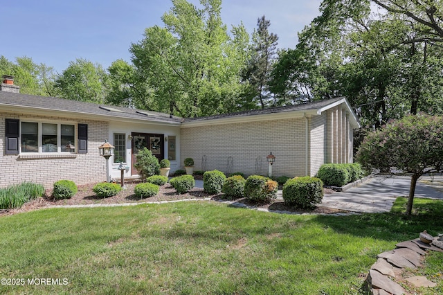 ranch-style house featuring a chimney, brick siding, and a front lawn