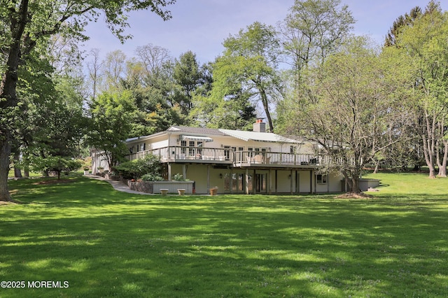 rear view of house featuring a chimney, a wooden deck, and a lawn