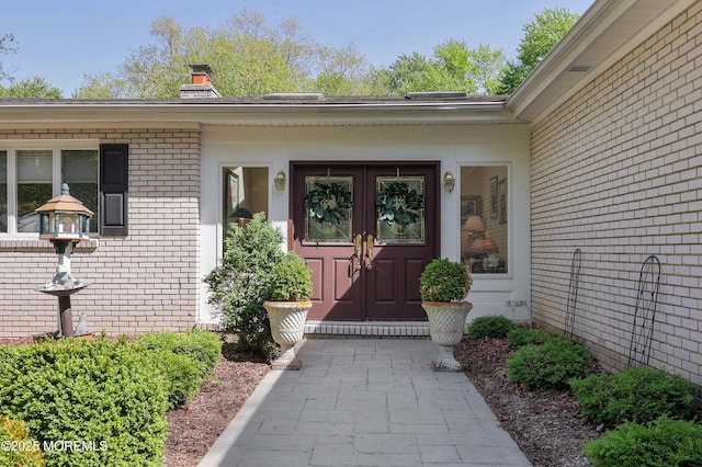 doorway to property featuring a chimney, french doors, and brick siding