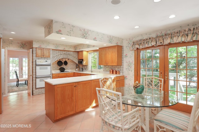kitchen featuring wallpapered walls, double oven, light tile patterned flooring, a peninsula, and light countertops