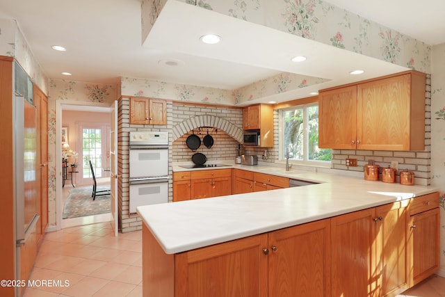 kitchen featuring a healthy amount of sunlight, white double oven, and wallpapered walls