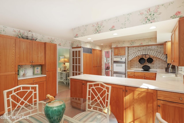 kitchen featuring wallpapered walls, double oven, light tile patterned flooring, a peninsula, and light countertops