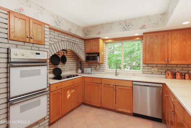 kitchen featuring a sink, stainless steel appliances, light countertops, decorative backsplash, and wallpapered walls