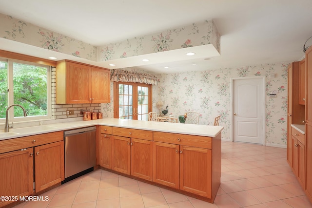 kitchen featuring a peninsula, light countertops, stainless steel dishwasher, and a sink