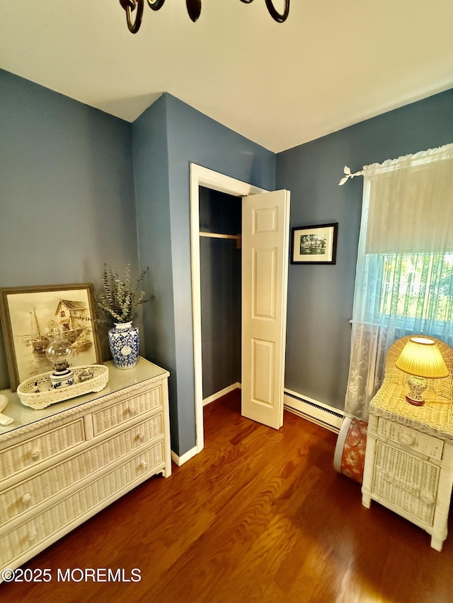 bedroom with a baseboard heating unit, wood finished floors, and baseboards