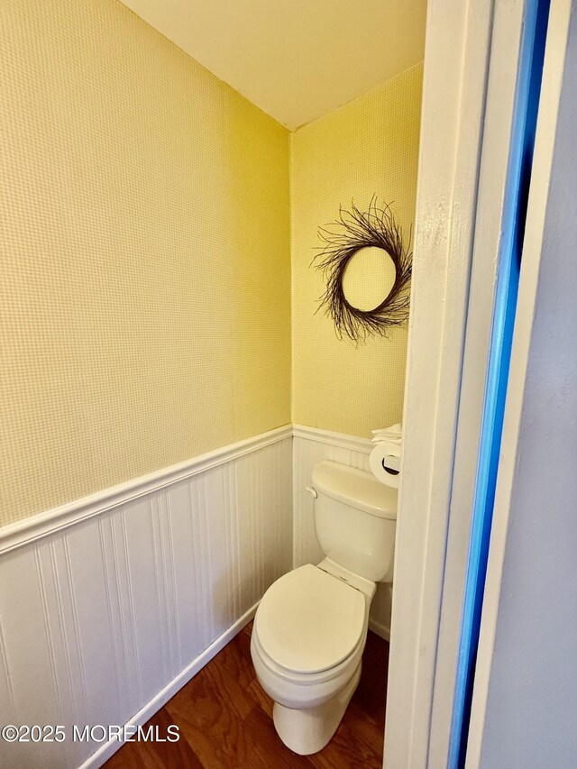 bathroom with wood finished floors, toilet, and a wainscoted wall