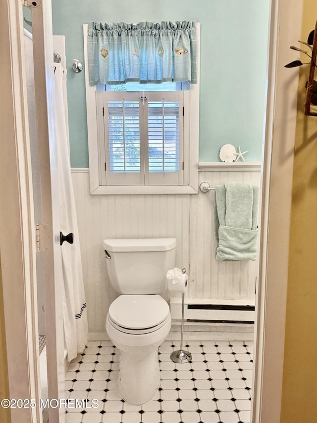bathroom featuring a wainscoted wall, toilet, tile patterned flooring, and a shower with curtain