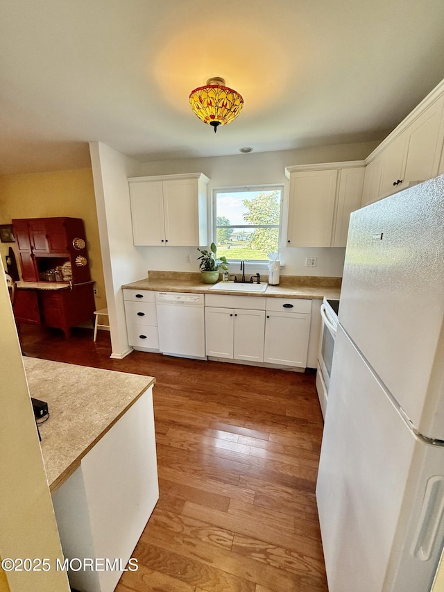 kitchen featuring white appliances, a sink, white cabinetry, light wood finished floors, and light countertops