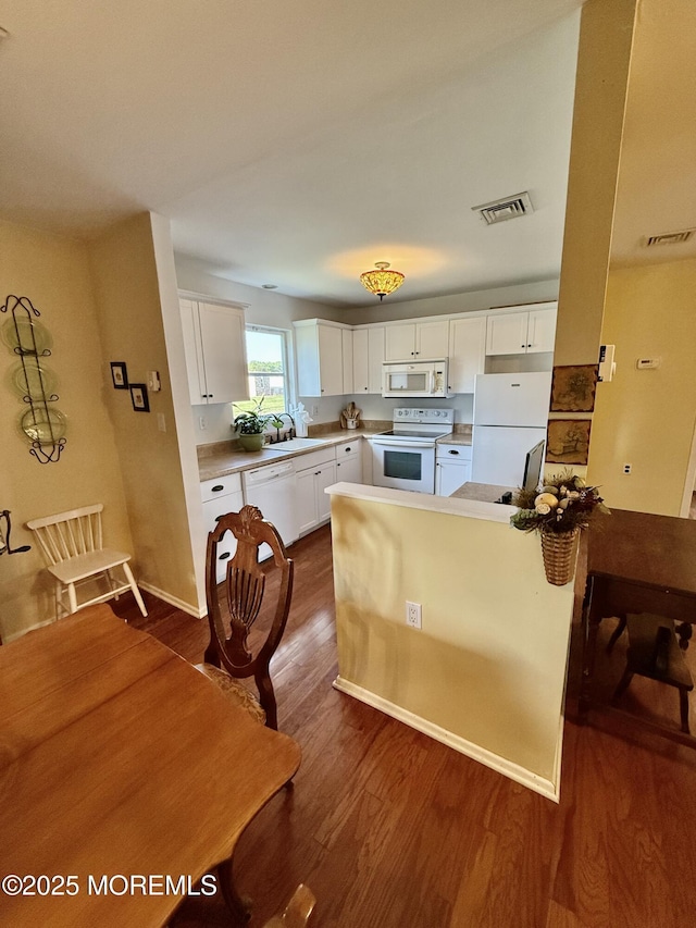 kitchen with white appliances, a sink, dark wood-style floors, white cabinets, and a peninsula