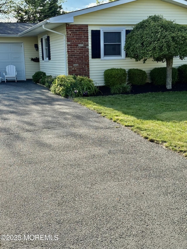 view of home's exterior featuring an attached garage, driveway, brick siding, and a lawn