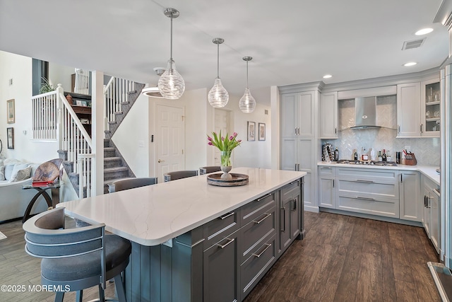 kitchen with decorative backsplash, dark wood-style flooring, visible vents, pendant lighting, and wall chimney exhaust hood