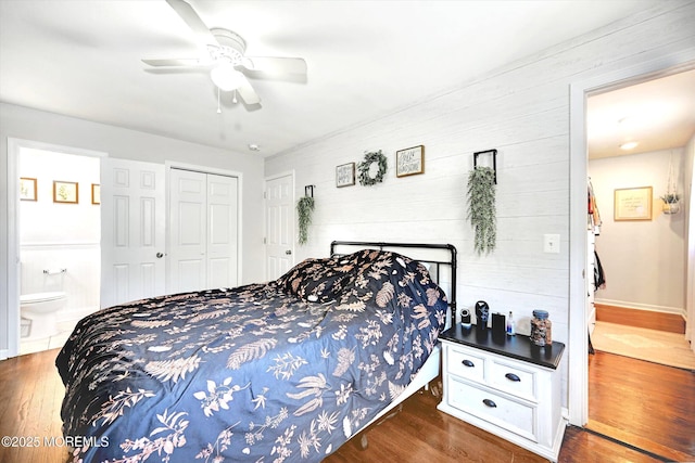 bedroom featuring wooden walls, a ceiling fan, wood finished floors, ensuite bathroom, and a closet