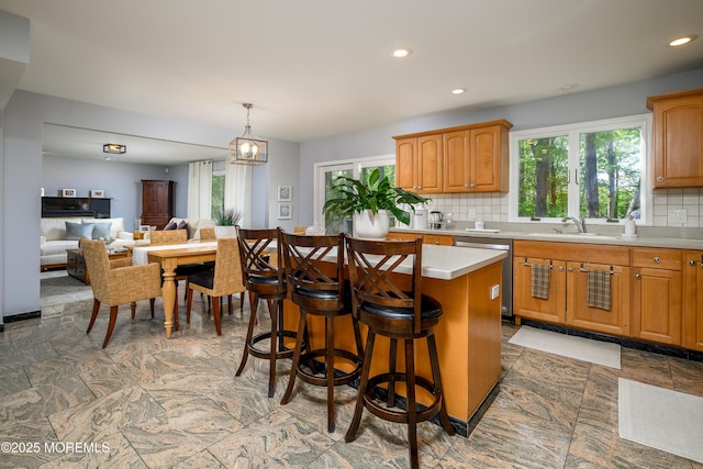 kitchen featuring stainless steel dishwasher, light countertops, tasteful backsplash, a sink, and a kitchen island