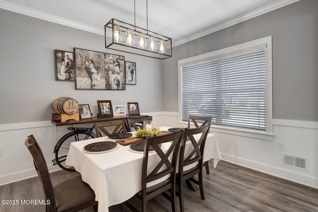 dining room featuring visible vents, ornamental molding, wainscoting, a decorative wall, and wood finished floors