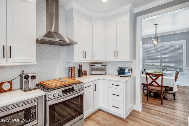 kitchen featuring wall chimney range hood, appliances with stainless steel finishes, white cabinets, and light countertops