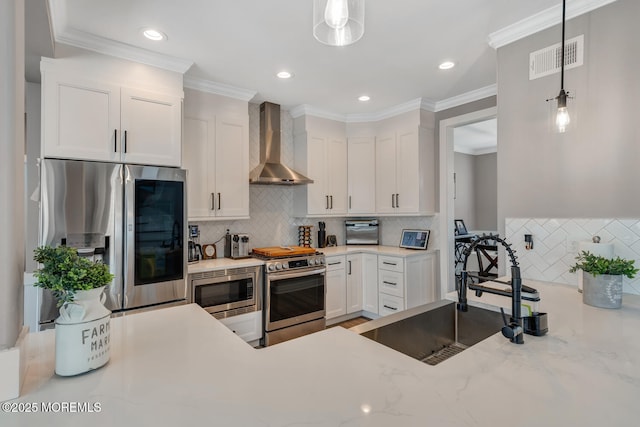 kitchen with appliances with stainless steel finishes, a sink, wall chimney exhaust hood, white cabinetry, and visible vents