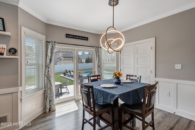 dining area with crown molding, a notable chandelier, plenty of natural light, and wood finished floors