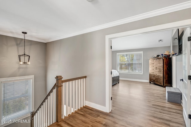 hallway featuring baseboards, ornamental molding, wood finished floors, and an upstairs landing