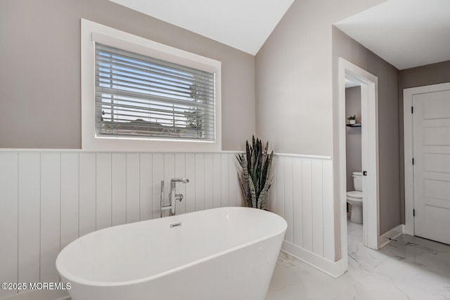 full bath with toilet, a freestanding bath, wainscoting, and marble finish floor