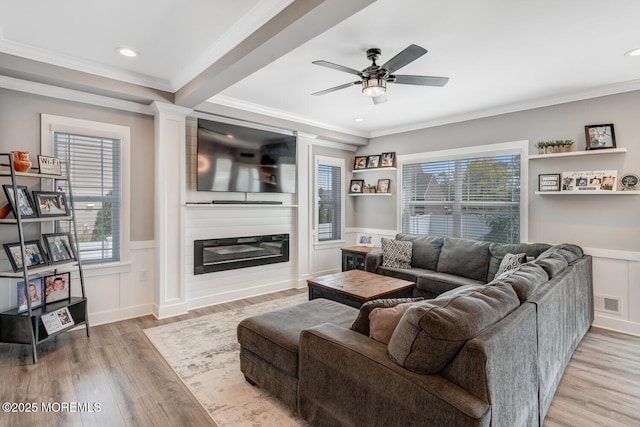 living area featuring ceiling fan, ornamental molding, light wood-style flooring, and a wainscoted wall