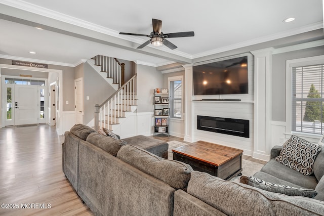 living room featuring light wood finished floors, ceiling fan, a wainscoted wall, and a decorative wall