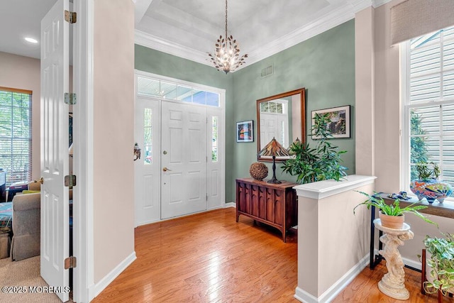 foyer featuring baseboards, light wood finished floors, healthy amount of natural light, ornamental molding, and a towering ceiling