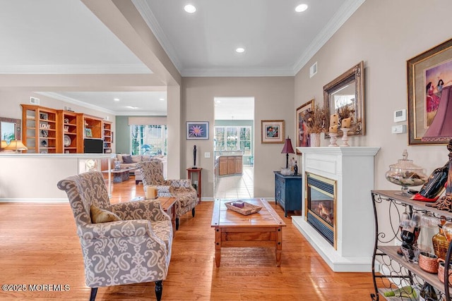 living area featuring ornamental molding, light wood-style floors, a glass covered fireplace, and recessed lighting