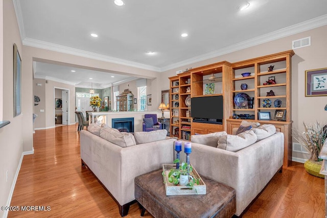 living room featuring light wood finished floors, ornamental molding, baseboards, recessed lighting, and a glass covered fireplace