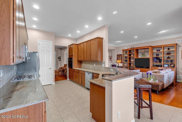 kitchen featuring a peninsula, appliances with stainless steel finishes, a sink, a kitchen bar, and light tile patterned flooring