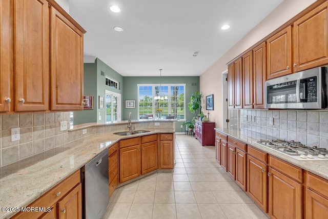 kitchen featuring appliances with stainless steel finishes, a sink, a peninsula, tasteful backsplash, and light stone countertops