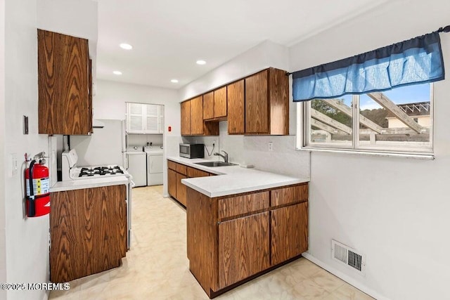 kitchen with visible vents, washing machine and clothes dryer, brown cabinets, a sink, and light countertops