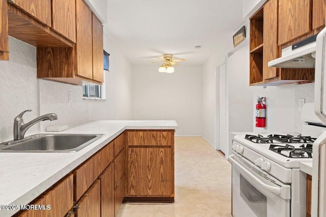 kitchen with white gas stove, a ceiling fan, a sink, light countertops, and a peninsula