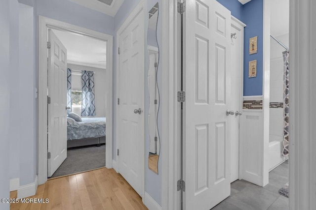 hall featuring crown molding, baseboards, and light wood-type flooring