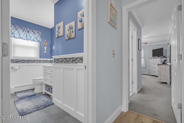 hallway with crown molding, a baseboard heating unit, wood finished floors, and a wainscoted wall
